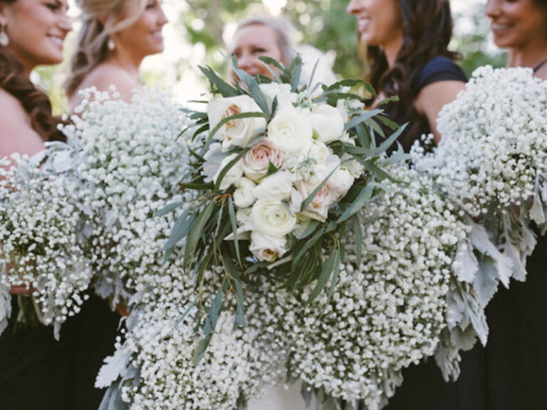 Bridesmaids holding white and blush bouquets with baby’s breath and greenery.